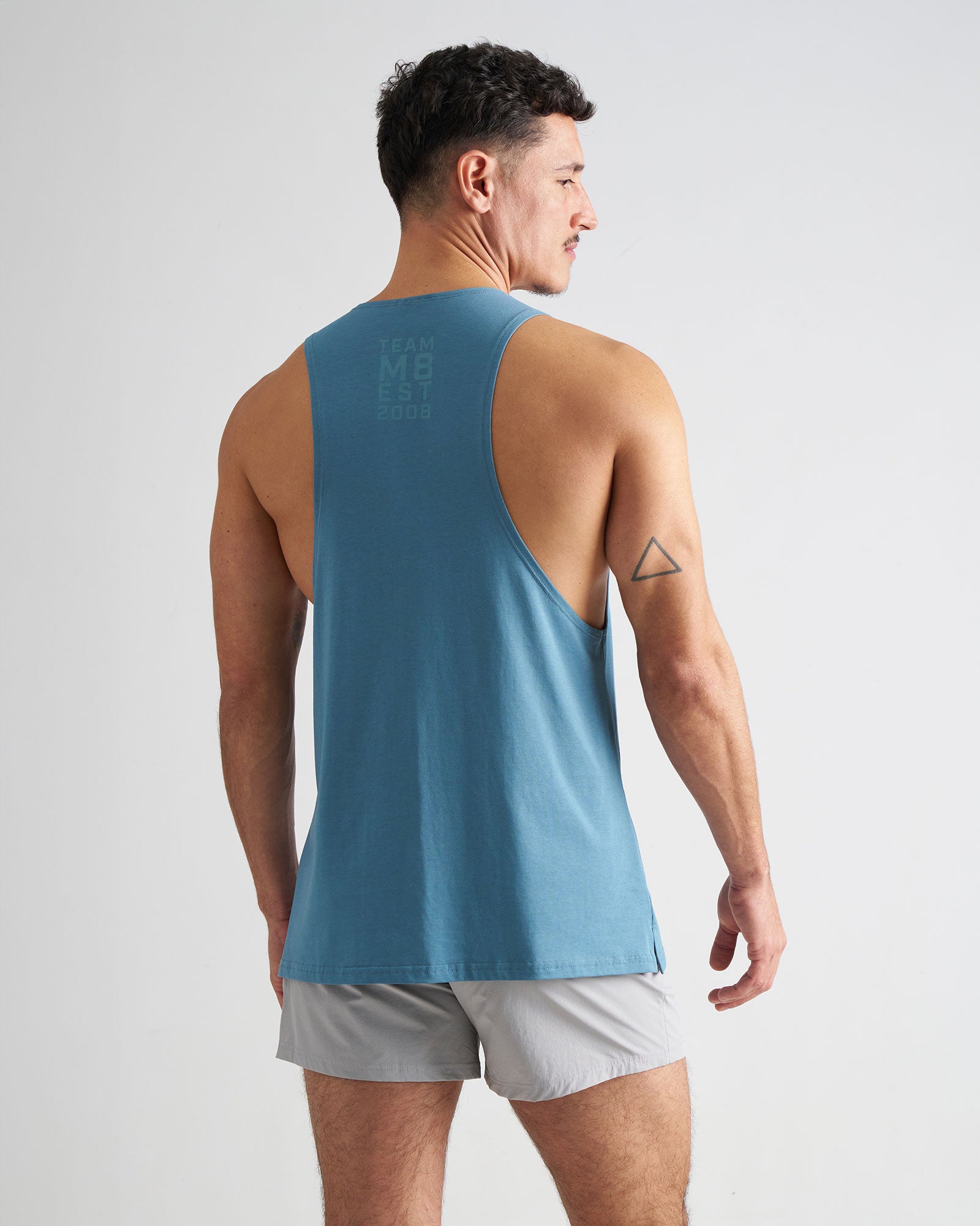 Man wearing a blue tank top and gray shorts on a light gray background