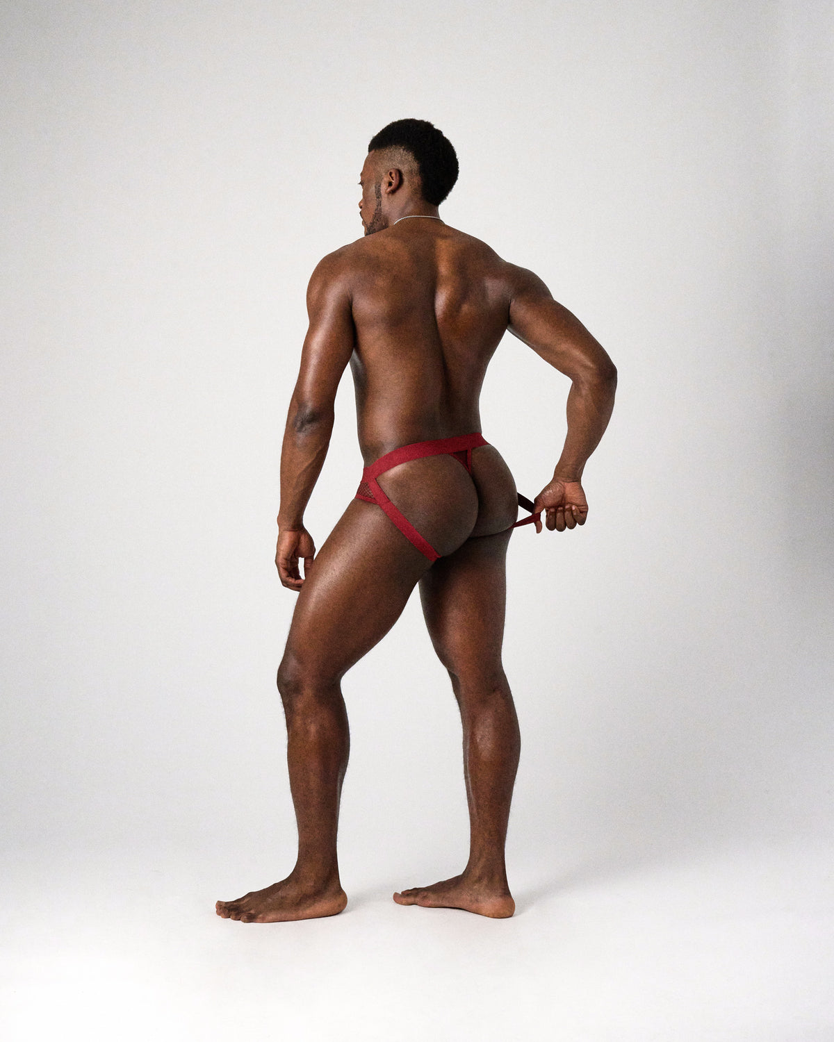 Edge Net Jock/Thong in Maroon, full-length back view as the model pulls a leg strap