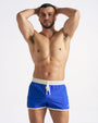 Man wearing blue swim shorts with a white waistband on a plain background