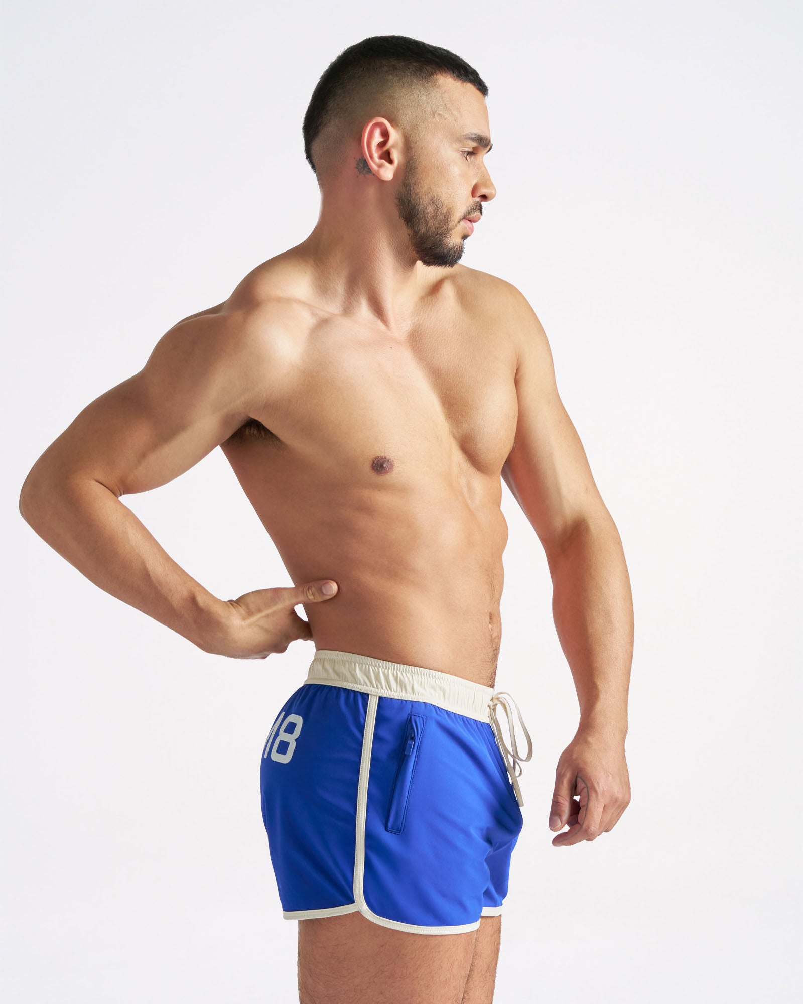 Man wearing blue swim shorts with a white waistband on a light gray background