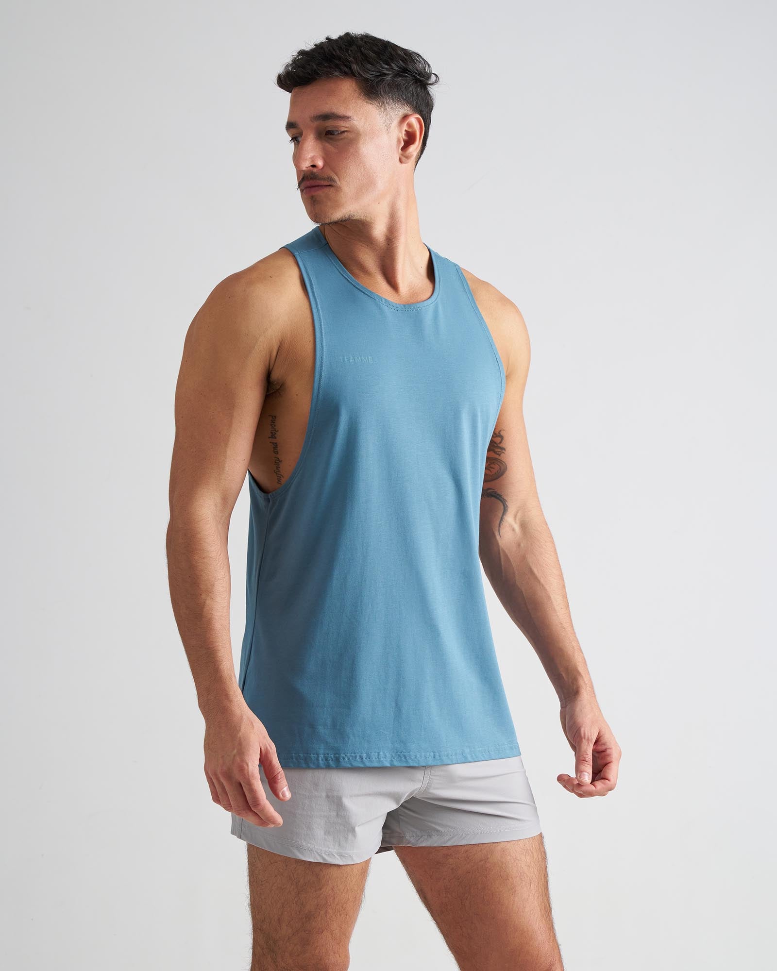 Man wearing a blue tank top and gray shorts on a light gray background