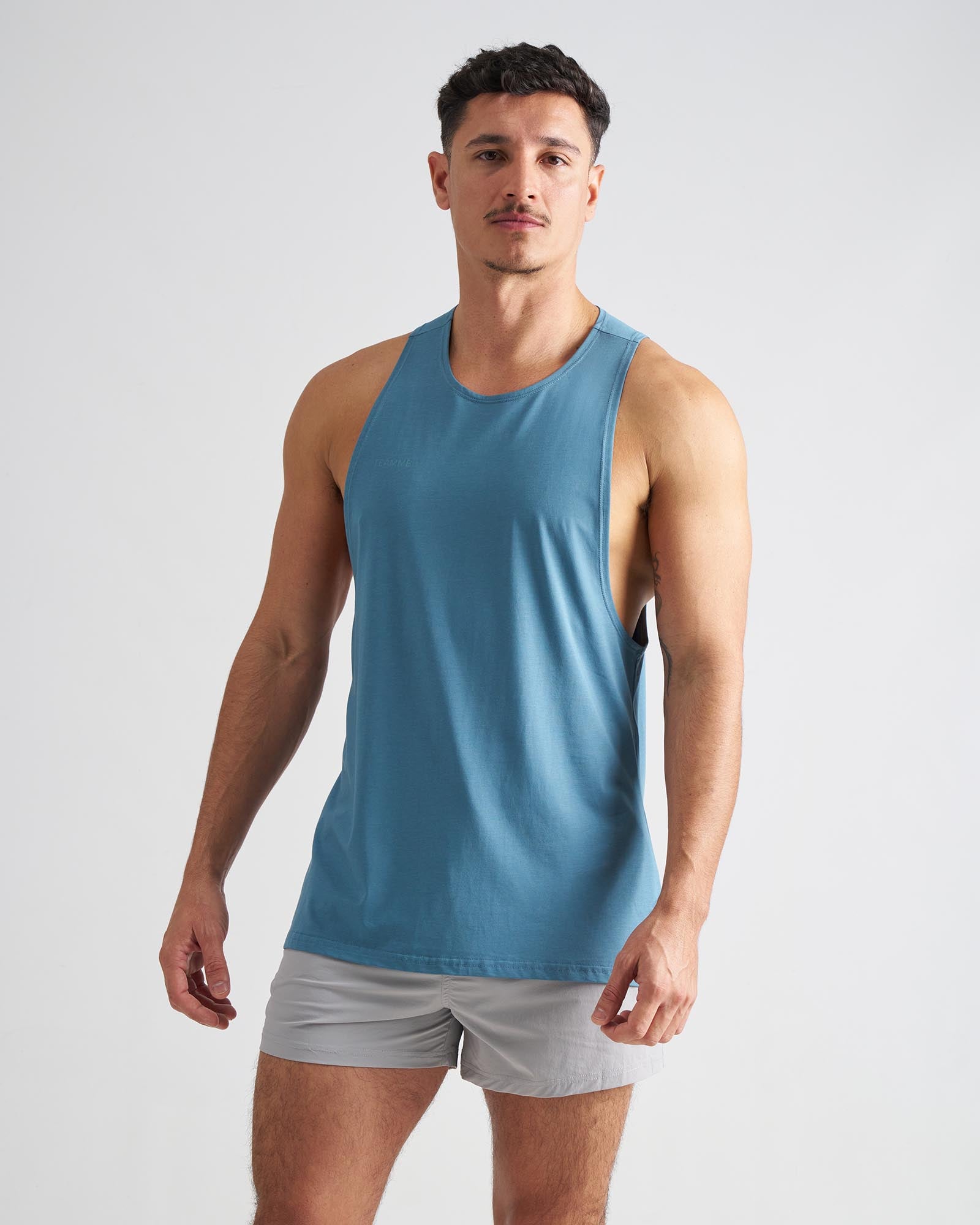 Man wearing a blue tank top and gray shorts on a white background